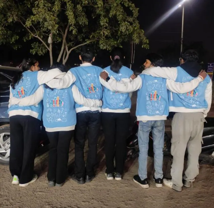 Six members photographed from behind at night, arms around each other in matching pale blue AIESEC letterman jackets.